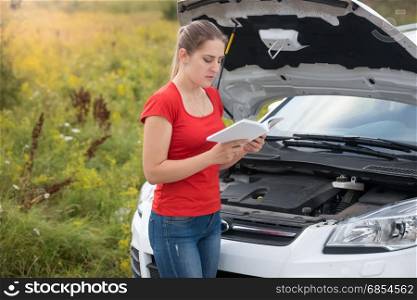 Woman reading owner manual at broken car in meadow
