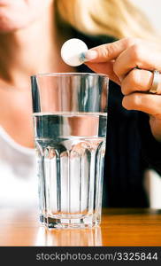 Woman ready to drop a pill into a glass of water (macro)