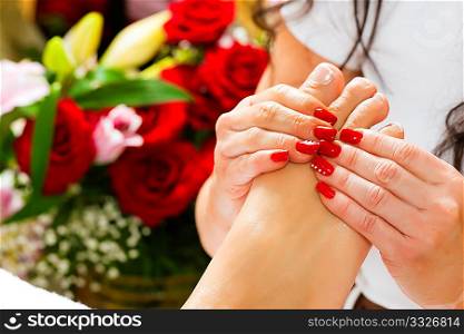 Woman receiving feet massage with massage in a Day Spa; lots of flowers in the background