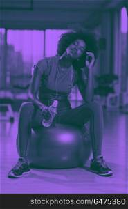 woman relaxing after pilates workout. happy african american woman with a curly afro hairstyle in a gym relaxing after pilates workout duo tone filter