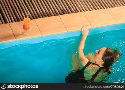 Woman relaxing at swimming pool edge. Leisure.. Woman in black dress relaxing at swimming pool edge poolside. Young girl with tropical drink cocktail resting. Leisure.