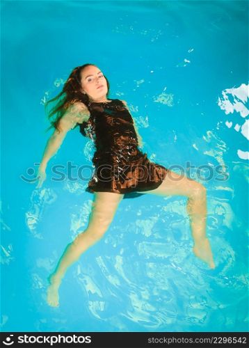 Woman relaxing at swimming pool. Young girl wearing black dress floating. Water aerobics fitness.. Woman floating relaxing in swimming pool water.