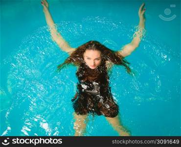 Woman relaxing at swimming pool. Young girl wearing black dress floating. Water aerobics fitness.. Woman floating relaxing in swimming pool water.