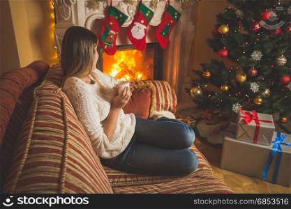 Woman relaxing by the fireplace and Christmas tree with cup of tea