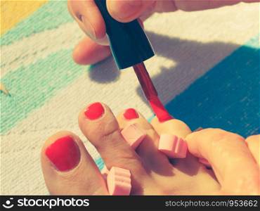 Woman relaxing doing her pedicure with red nail polish on beach towel. Female taking care of feet. Woman pedicure with red nail polish
