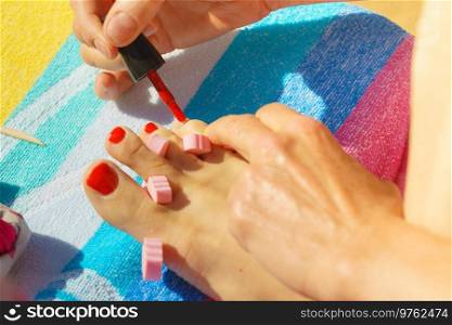 Woman relaxing doing her pedicure with red nail polish on beach towel. Female taking care of feet. Woman pedicure with red nail polish