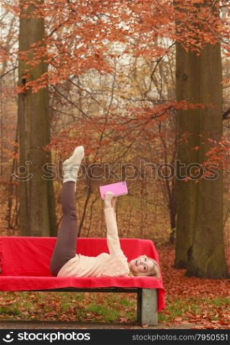 Woman relaxing in autumn fall park reading book.. Carefree woman relaxing in fall park reading book. Young blonde girl having fun resting laying on bench. Autumn lifestyle.
