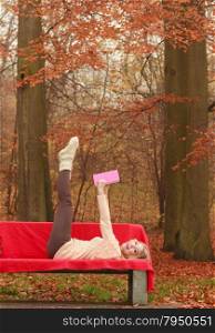 Woman relaxing in autumn fall park reading book.. Carefree woman relaxing in fall park reading book. Young blonde girl having fun resting laying on bench. Autumn lifestyle.