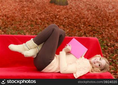 Woman relaxing in autumn fall park with book.. Happy smiling woman relaxing in fall park with book. Young blonde girl resting laying on bench. Autumn lifestyle fun.