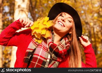 Woman relaxing in autumn fall park. Young feshionable female stylish black hat holding yellow maple leaves in hand, enjoying sunlight. Woman relaxing in autumn fall park