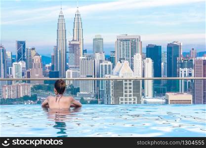 Woman relaxing in infinity swimming pool roof top looking at beautiful city skyscraper view Kuala lumpur, Malaysia