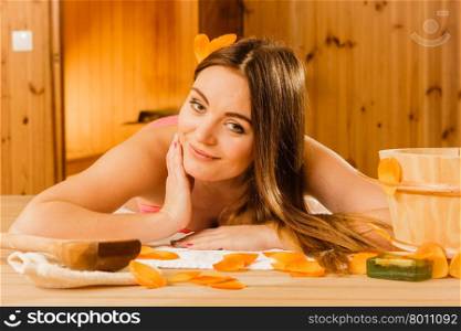 Woman relaxing in sauna. Spa wellbeing.. Woman with bucket ladle and petals relaxing in finnish sauna. Attractive girl in bikini resting. Spa wellbeing pleasure.