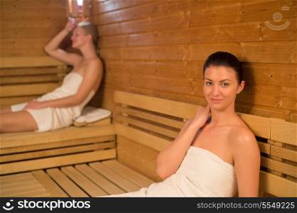Woman relaxing in sauna with friend in background