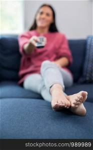 Woman Relaxing On Sofa Holding Remote Control And Watching Television
