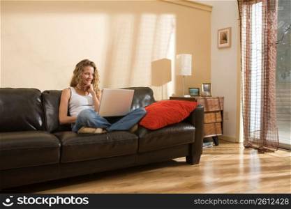 Woman relaxing on sofa in living room using laptop
