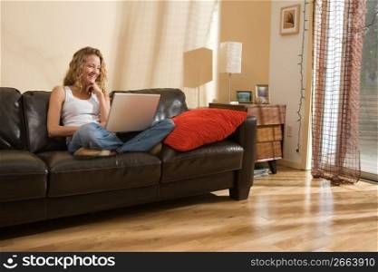 Woman relaxing on sofa in living room using laptop