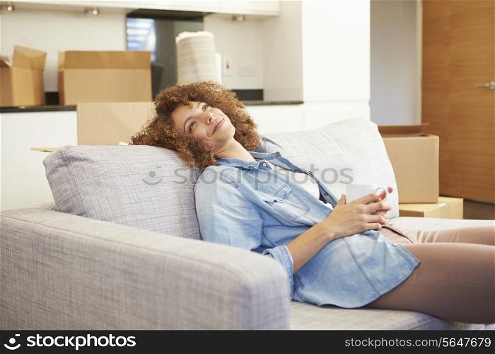 Woman Relaxing On Sofa With Hot Drink In New Home