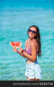 Woman relaxing on the beach on a summer day smiling with a slice of watermelon in her hand. Happy girl having fun on the beach and eating watermelon
