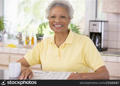 Woman relaxing with newspaper in kitchen and smiling