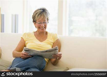 Woman relaxing with newspaper in living room smiling