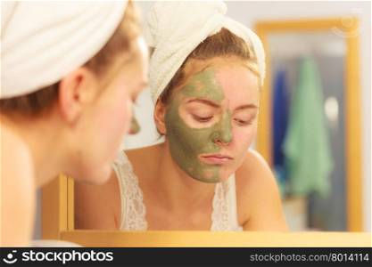 Woman removing facial clay mud mask in bathroom. Woman removing facial dried clay mud mask with sponge in bathroom in front of mirror. Skin care. Girl taking care of her complexion. Beauty spa treatment.