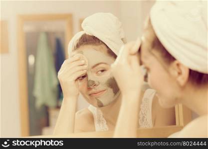 Woman removing facial clay mud mask in bathroom. Woman removing facial dried clay mud mask with sponge in bathroom in front of mirror. Skin care. Girl taking care of her complexion. Beauty spa treatment.