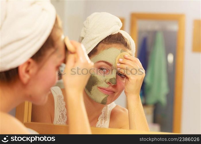 Woman removing facial dried clay mud mask with sponge in bathroom in front of mirror. Skin care. Girl taking care of her complexion. Beauty spa treatment.. Woman removing facial clay mud mask in bathroom
