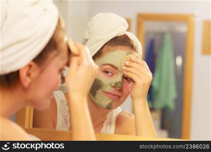 Woman removing facial dried clay mud mask with sponge in bathroom in front of mirror. Skin care. Girl taking care of her complexion. Beauty spa treatment.. Woman removing facial clay mud mask in bathroom