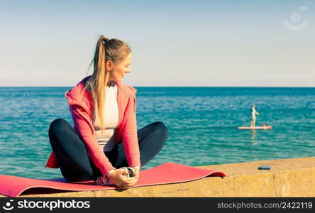 Woman resting relaxing after doing sports outdoors. Fitness girl female in sportswear on seaside takes break. Woman resting relaxing after doing sports outdoors