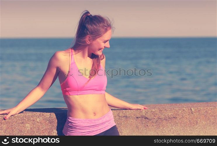 Woman resting relaxing after doing sports outdoors. Fitness girl female in sportswear on seaside takes break. Woman resting relaxing after doing sports outdoors