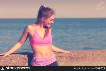 Woman resting relaxing after doing sports outdoors. Fitness girl female in sportswear on seaside takes break. Woman resting relaxing after doing sports outdoors