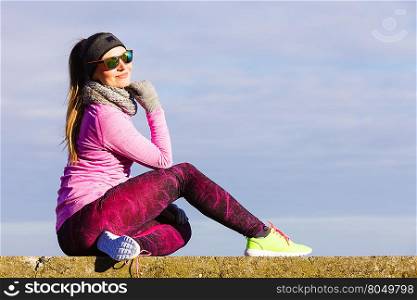 Woman resting relaxing after doing sports outdoors. Fitness girl female jogger wearing warm sporty clothes in cold day weather on seaside taking break, enjoying sunlight