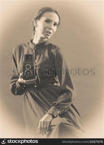Woman retro style long dark gown taking picture with old camera, vintage photo sepia tone