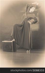 Woman retro style long dark gown with old suitcase and feather fan, vintage photo