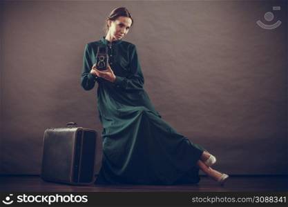 Woman retro style long dark green gown old suitcase and camera, taking picture vintage photo