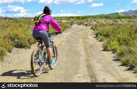 Woman riding a mountain bike by a muddy path of dirt. Healthy sport on the contryside.. Woman riding a mountain bike by a muddy path of dirt.