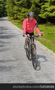 Woman riding mountain bike on sunny cycling path in forest