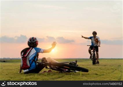 Woman riding mountain bike was accident crashed and fell to the grass while a lover her coming in to help at the beautiful sunset time. Using help and giving family love concept.