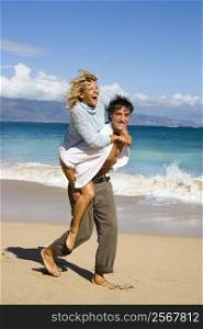 Woman riding piggyback on man while both smile and laugh on Maui, Hawaii beach.