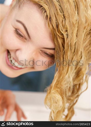 Woman rinsing her hair, washing out of shampoo having wet blonde hairdo in bathroom.. Woman having wet blonde hair