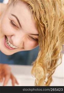 Woman rinsing her hair, washing out of shampoo having wet blonde hairdo in bathroom.. Woman having wet blonde hair
