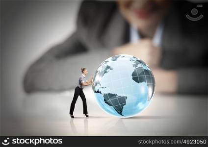 Woman rolling planet. Businesswoman looking at miniature of woman rolling globe