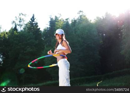woman rotates hula hoop on nature background