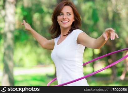 Woman rotates hula hoop on nature background