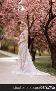 woman&rsquo;s day. beautiful young woman in luxury long dress near blossoming of sakura. stylish girl near blossoming sakura flowers on background in the spring park. Harmony with nature concept.. woman&rsquo;s day. beautiful young woman in luxury long dress near blossoming of sakura. stylish girl near blossoming sakura flowers on background in the spring park. Harmony with nature concept