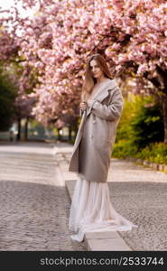 woman&rsquo;s day. beautiful young woman in luxury long dress near blossoming of sakura. stylish girl near blossoming sakura flowers on background in the spring park. Harmony with nature concept.. woman&rsquo;s day. beautiful young woman in luxury long dress near blossoming of sakura. stylish girl near blossoming sakura flowers on background in the spring park. Harmony with nature concept