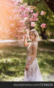 woman&rsquo;s day. beautiful young woman in luxury long dress near blossoming of sakura. stylish girl near blossoming sakura flowers on background in the spring park. Harmony with nature concept.. woman&rsquo;s day. beautiful young woman in luxury long dress near blossoming of sakura. stylish girl near blossoming sakura flowers on background in the spring park. Harmony with nature concept