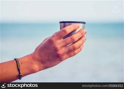 Woman&rsquo;s hand holding a cup by the sea