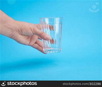 woman's hand holding an empty transparent glass, blue background