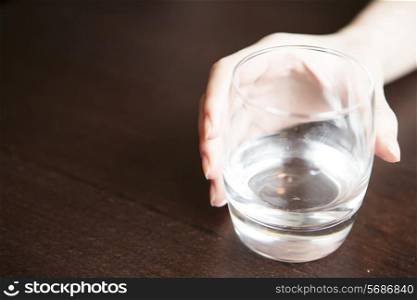 Woman&rsquo;s hand holding glass of water on table